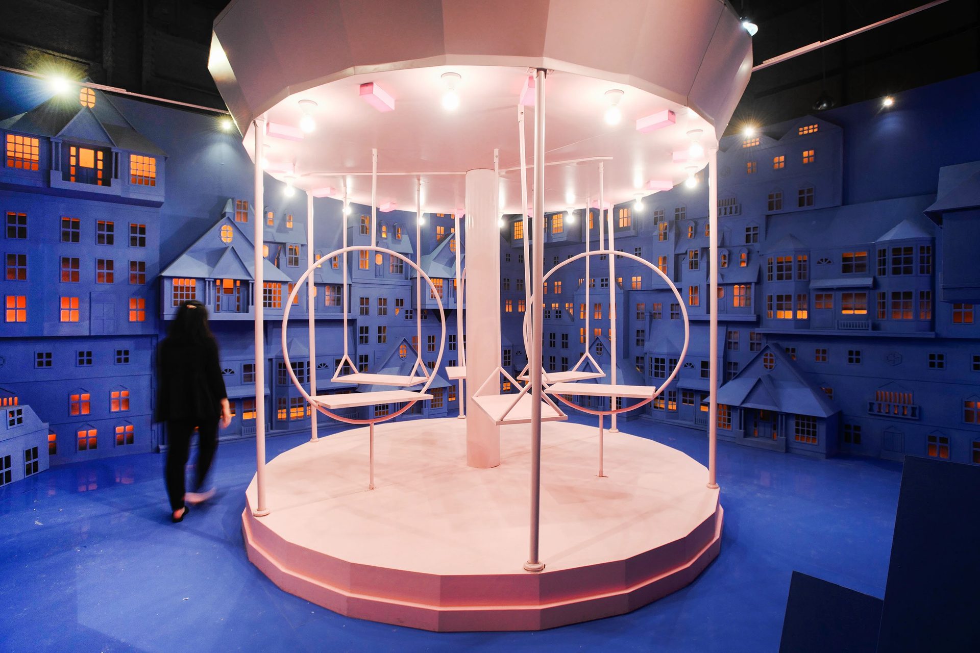 Pink carousel with swing seats in a paper city of blue houses