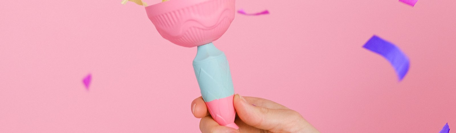 A hand holding a pink sculptural object against a pink backdrop