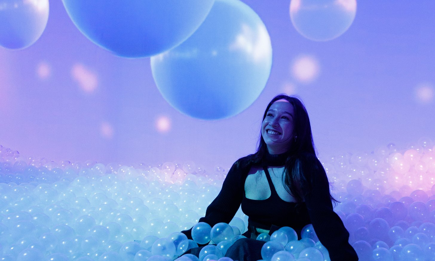 A performer surrounded by pale blue balloons under violet lighting