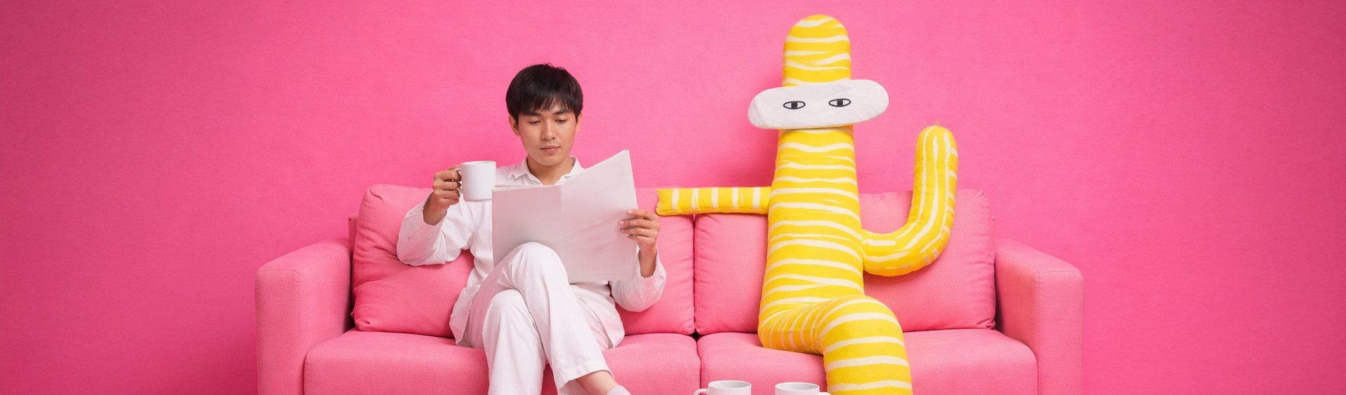 A man reading on a pink sofa beside a yellow striped HALUU mascot