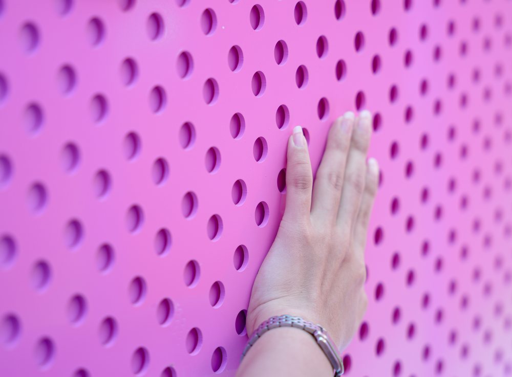 Hand pressing against a pink perforated textured wall